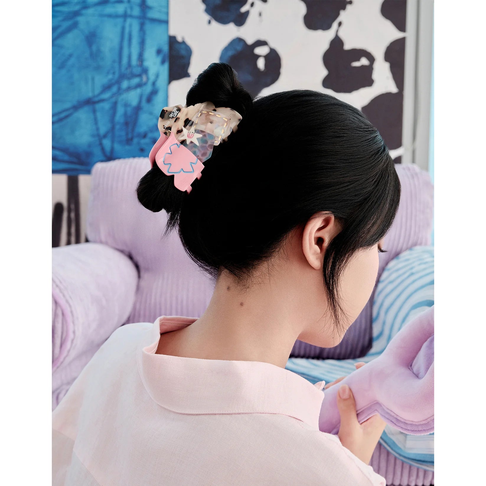 Person wearing a traditional hairstyle with decorative hairpin in front of a colorful abstract painting.