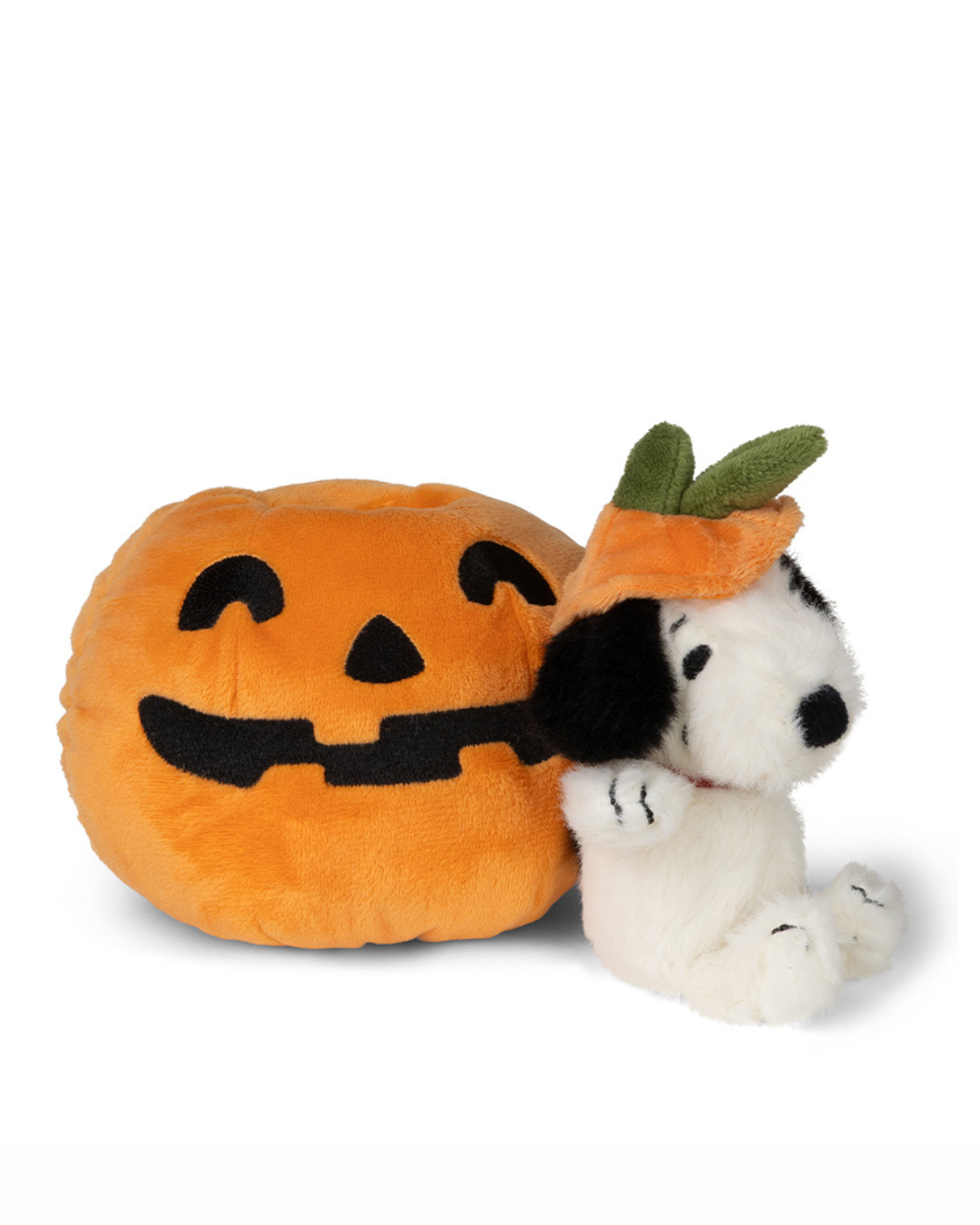 A plush toy featuring Snoopy wearing an orange pumpkin hat with green leaves, sitting next to a large orange pumpkin pillow with a black jack-o'-lantern face, on a white background.