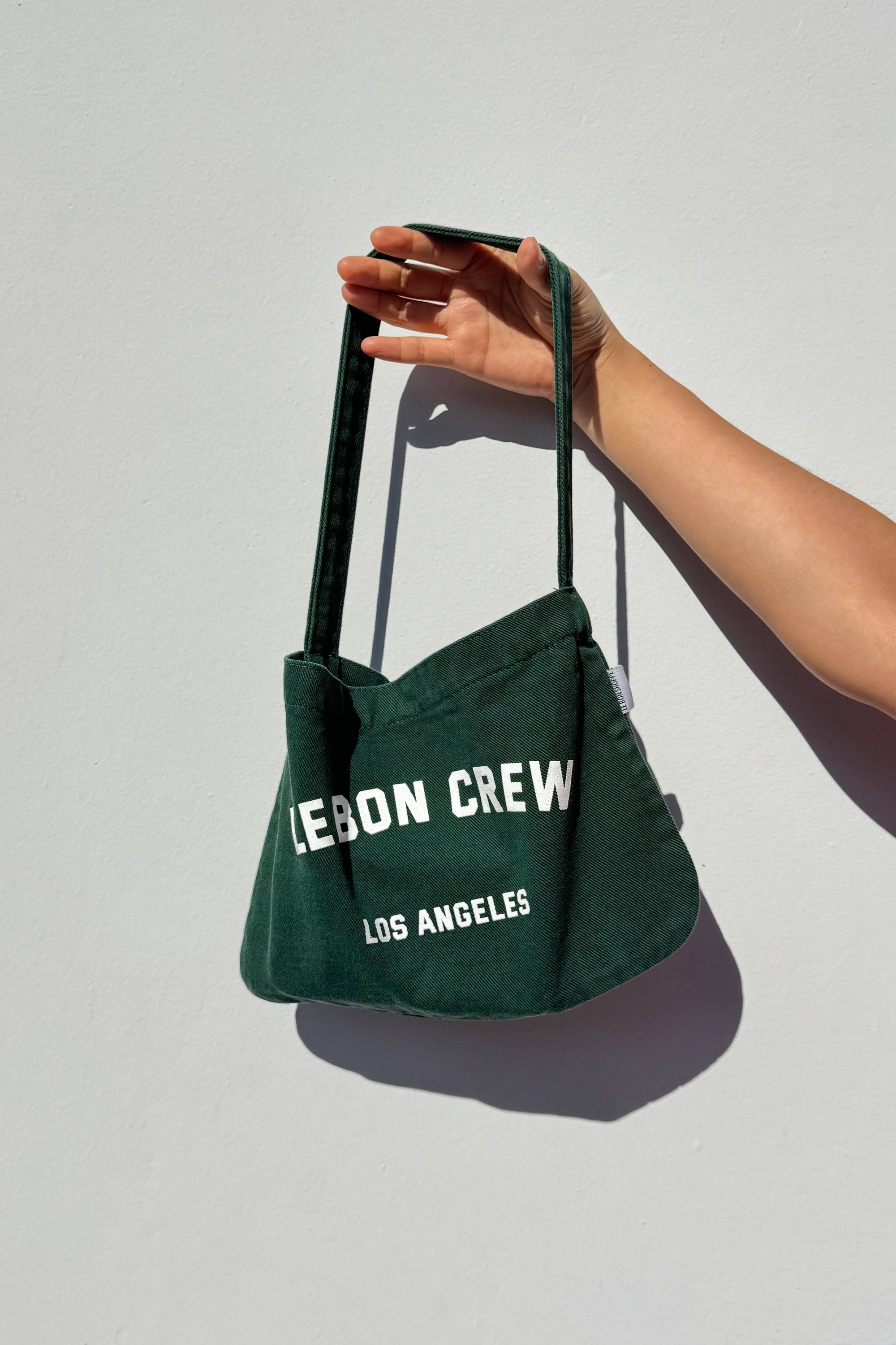 Green tote bag with 'Legion Crew Los Angeles' text held by a hand against a light gray background